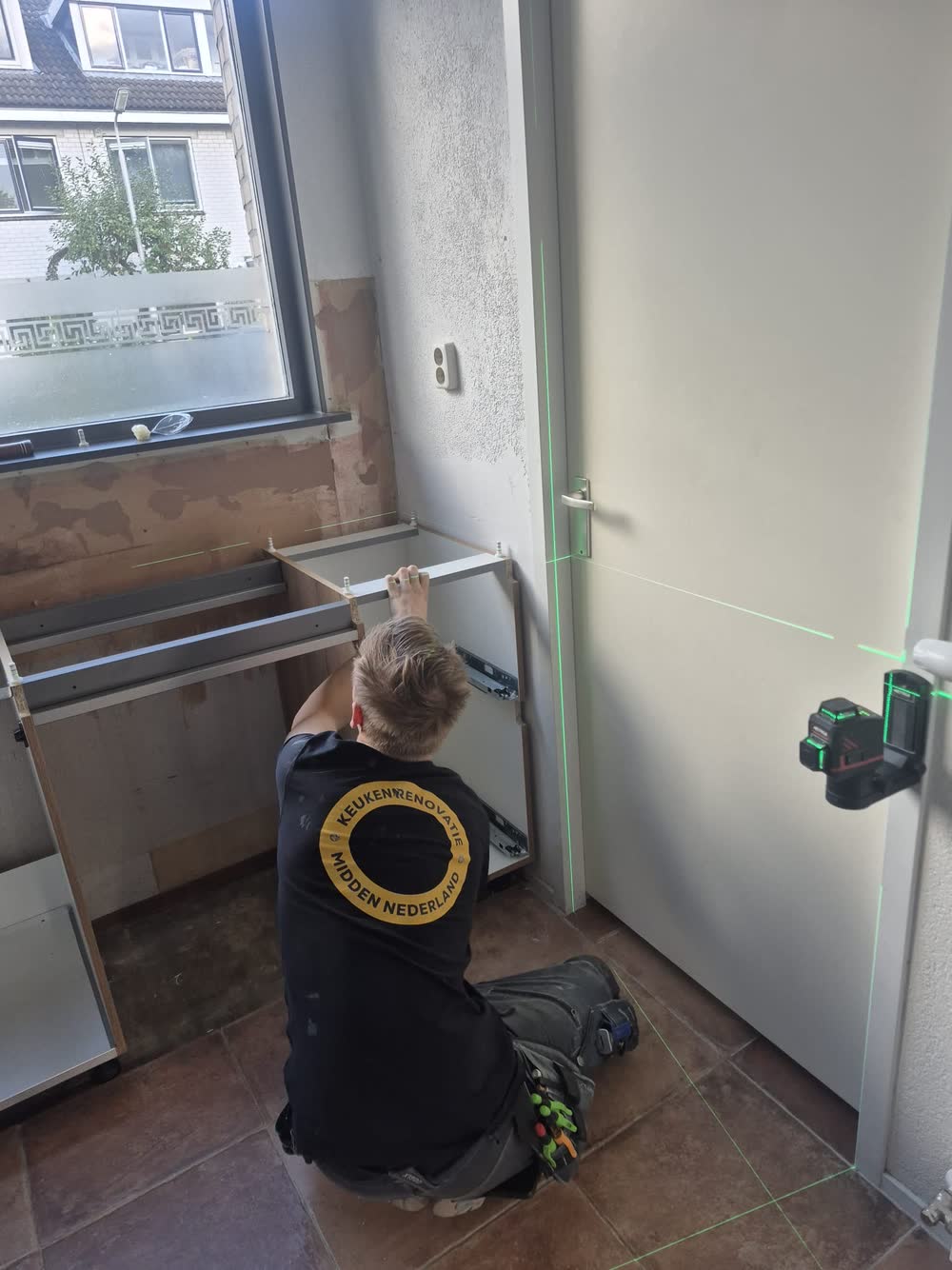 Een monteur stelt de onderkasten van een keuken waterpas langs de lijn van een laser