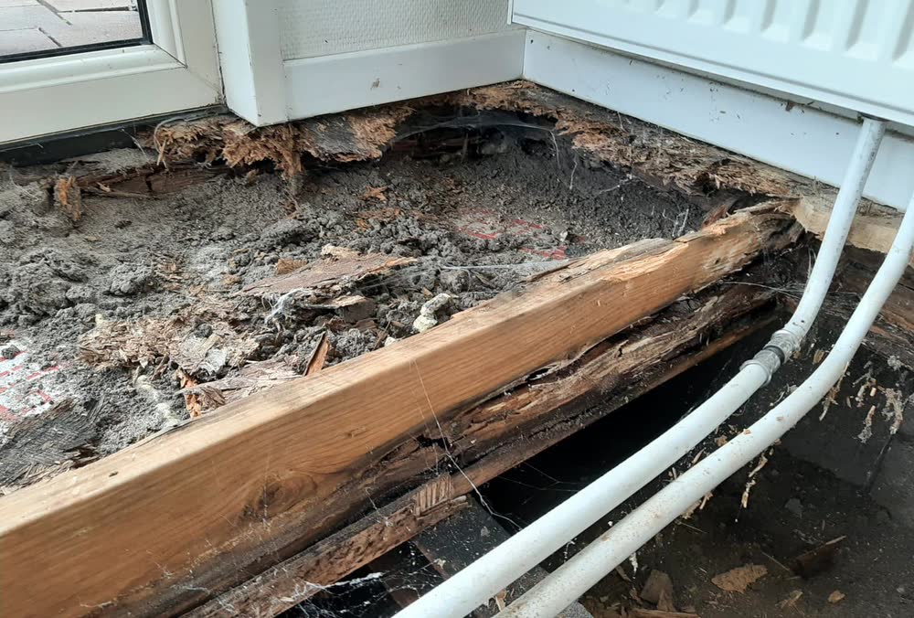 Verrot hout van de vloerbalk onder de pui, uit elkaar gevallen tot vezels