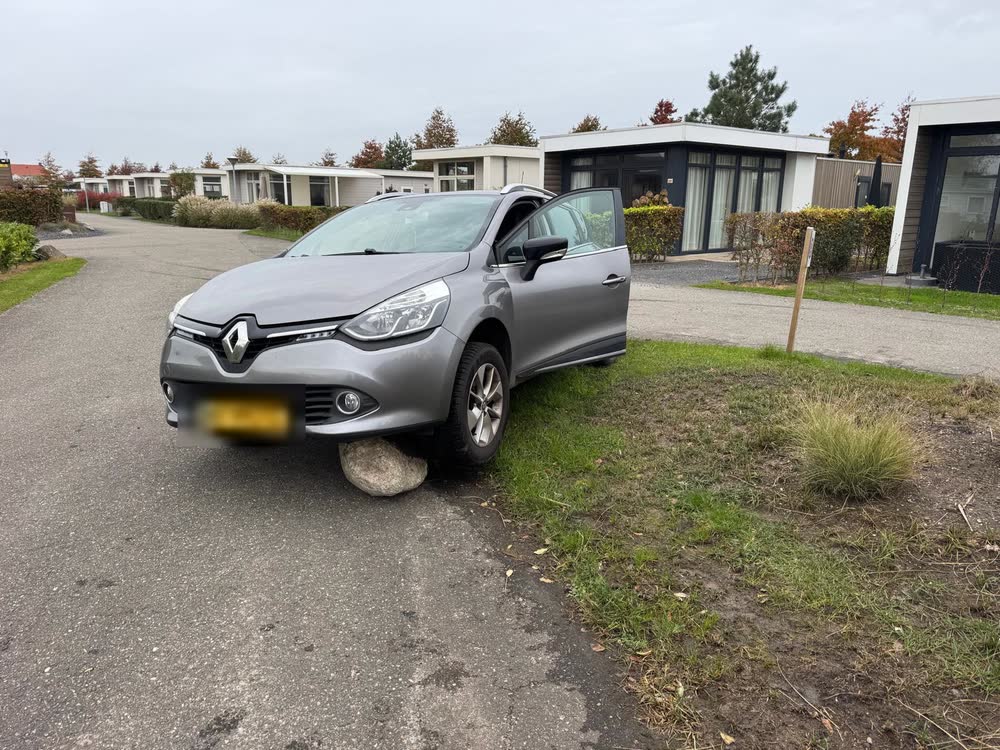 Een grijze auto staat met het voorwiel op een grote steen naast de weg in Nunspeet; het kenteken is onleesbaar gemaakt