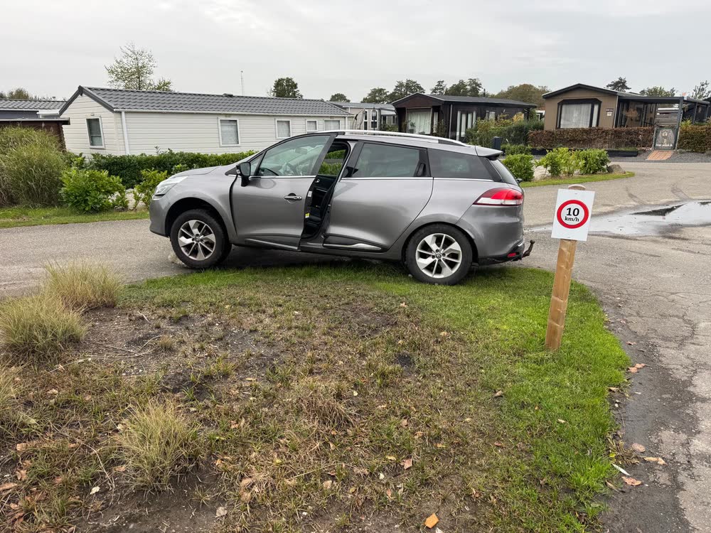 Zijaanzicht van de auto die schuin op de steen in de berm hangt, met het portier open