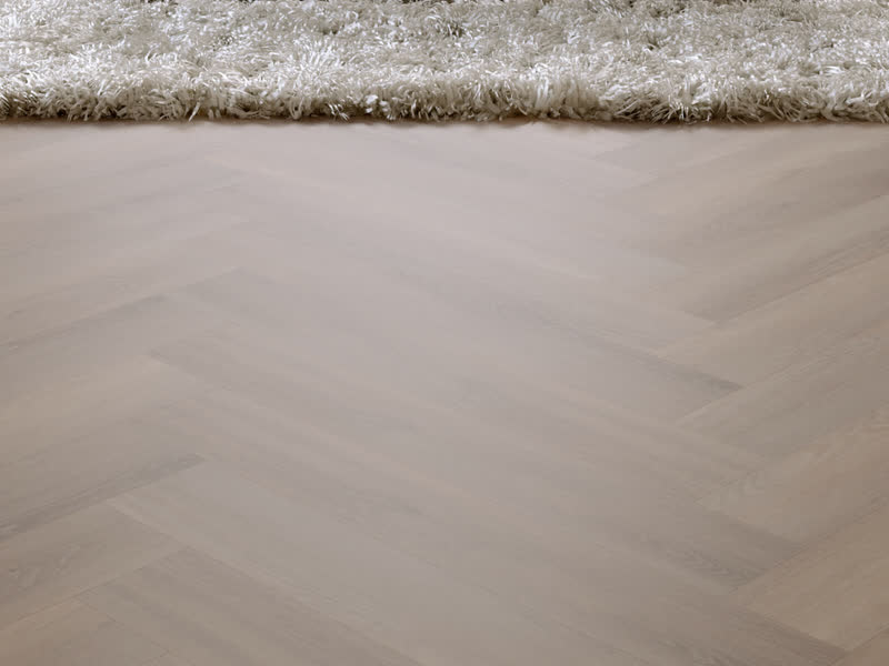 Dichtbij: de lichte visgraat van Room5 Ambassador Oak met de rand van een hoogpolig kleed