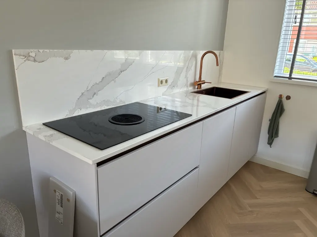 Witte keuken met een achterwand in marmerlook en een koperen kraan